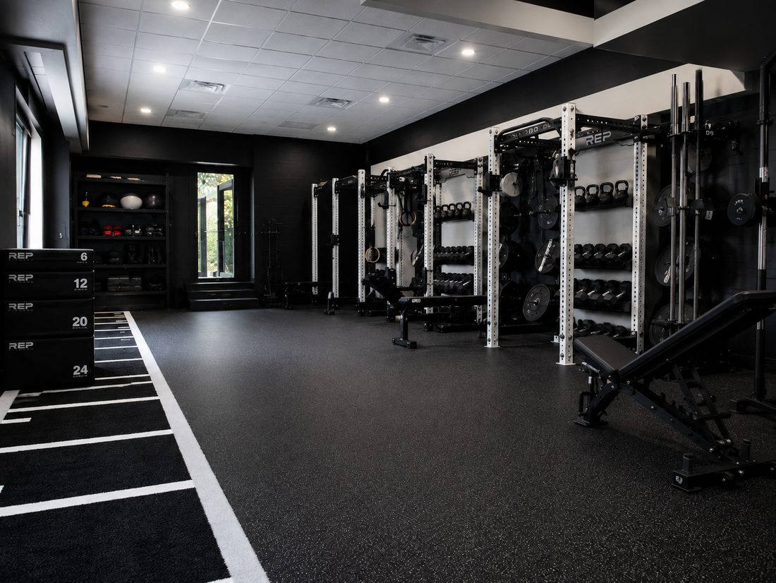 Home gym with black rubber flooring, racks, and a turf lane