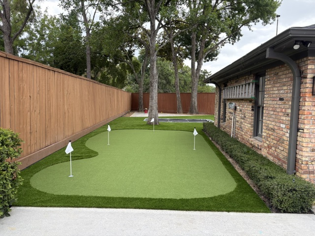 Curved backyard putting green beside a pool next to a brick home