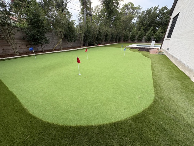 Large multi-hole putting green with colored flags behind a home