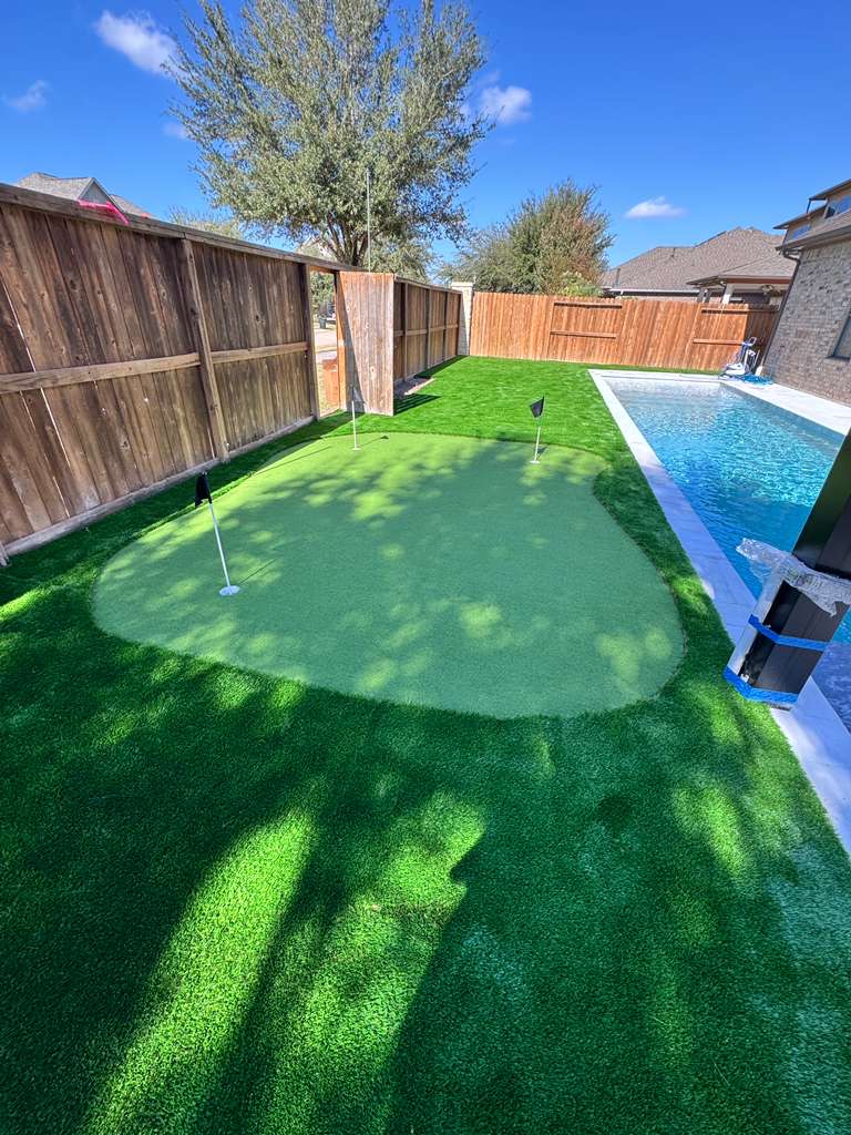 Single-hole putting green beside a pool with a wood privacy fence